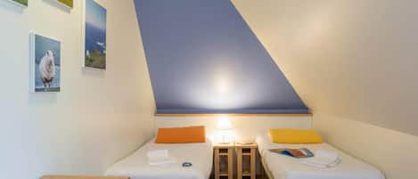 Una habitación pequeña y triangular con dos camas, un escritorio y una lámpara.