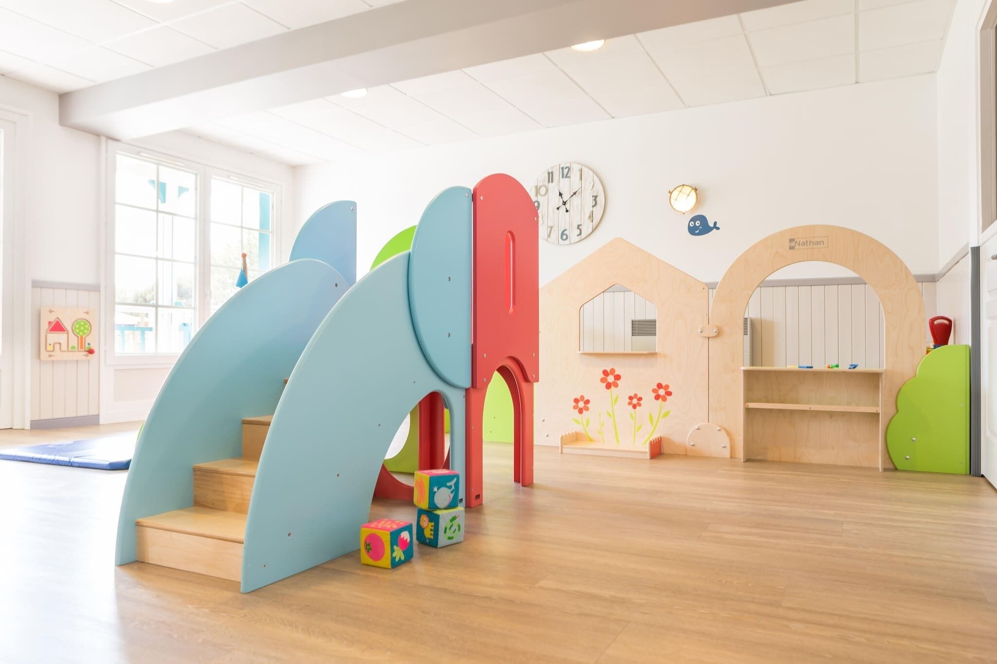 A children's play area with a slide, colorful blocks, and a clock on the wall.