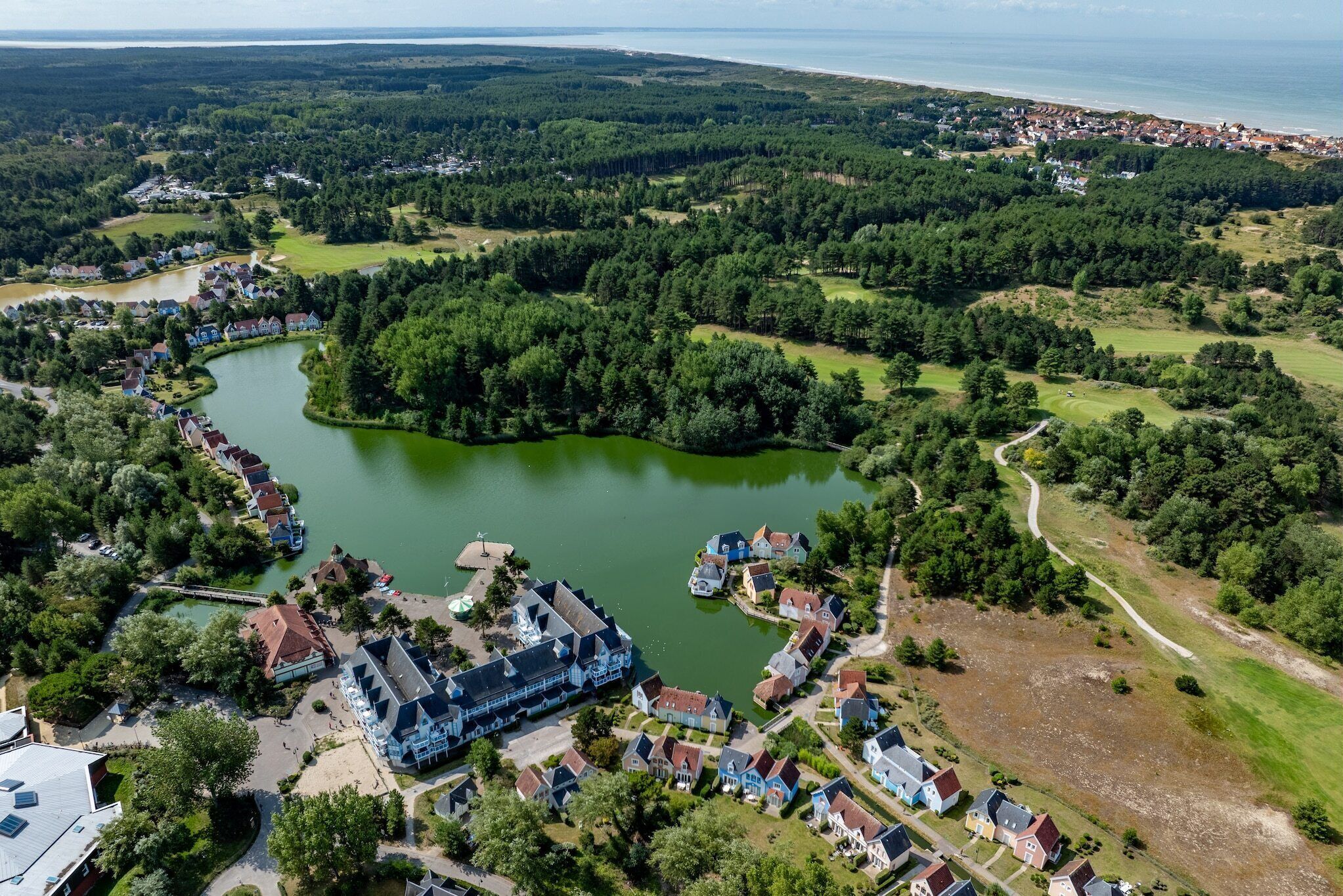 Une vue aérienne d’une communauté riveraine, avec des maisons, un grand bâtiment et une plage en arrière-plan.