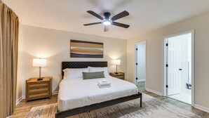 A bedroom with a bed, two bedside tables, a ceiling fan, a painting, and a door leading to another room. - Easy Access to Dtwn & Fort Benning: Family Home (Columbus)