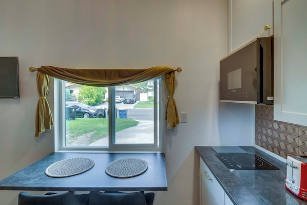 Eine Küche mit Fenster, Tisch mit Platzsets, einem Toaster und einer gemusterten Spritzschutzleiste.