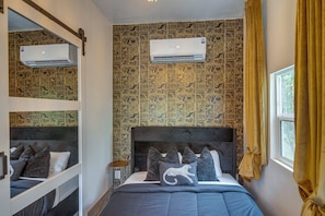 Ein Zimmer mit einem Etagenbett, einem großen Bett mit vielen Kissen, einer Klimaanlage und Wandpapier mit Muster.