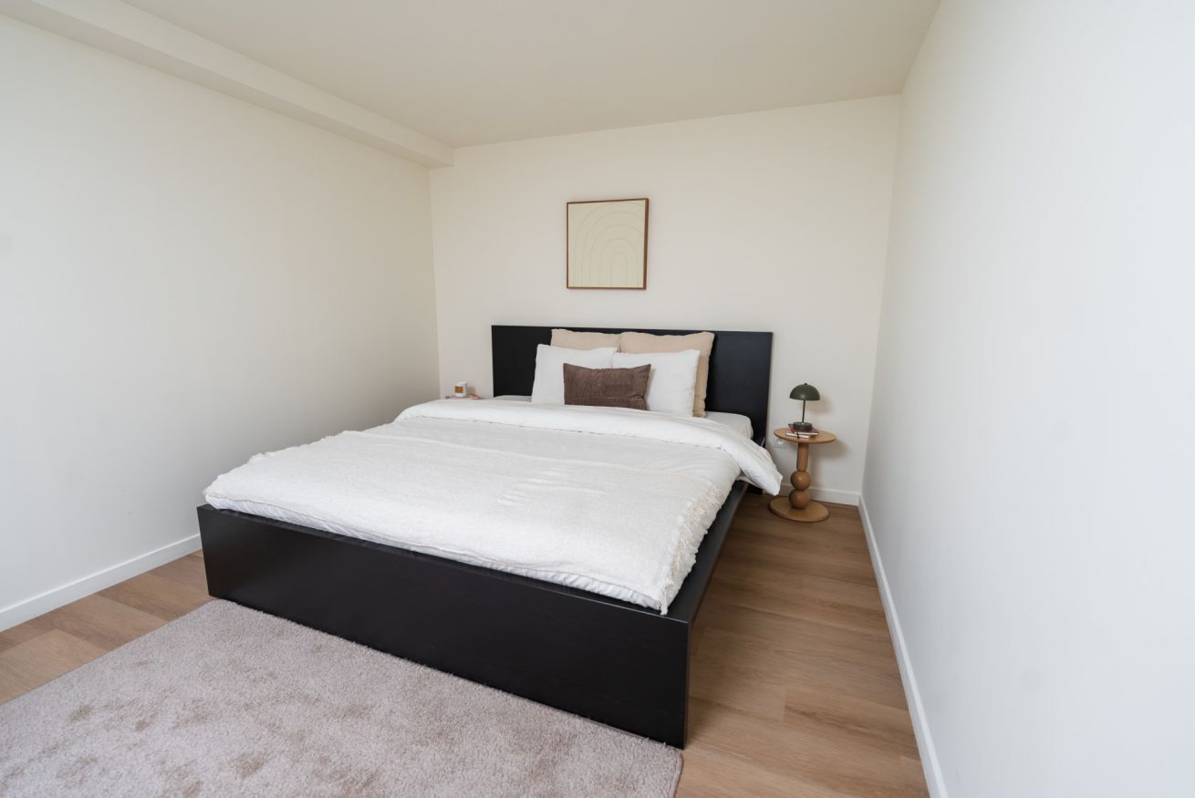 A bedroom with a bed, a bedside table, a lamp, and a framed picture on the wall.