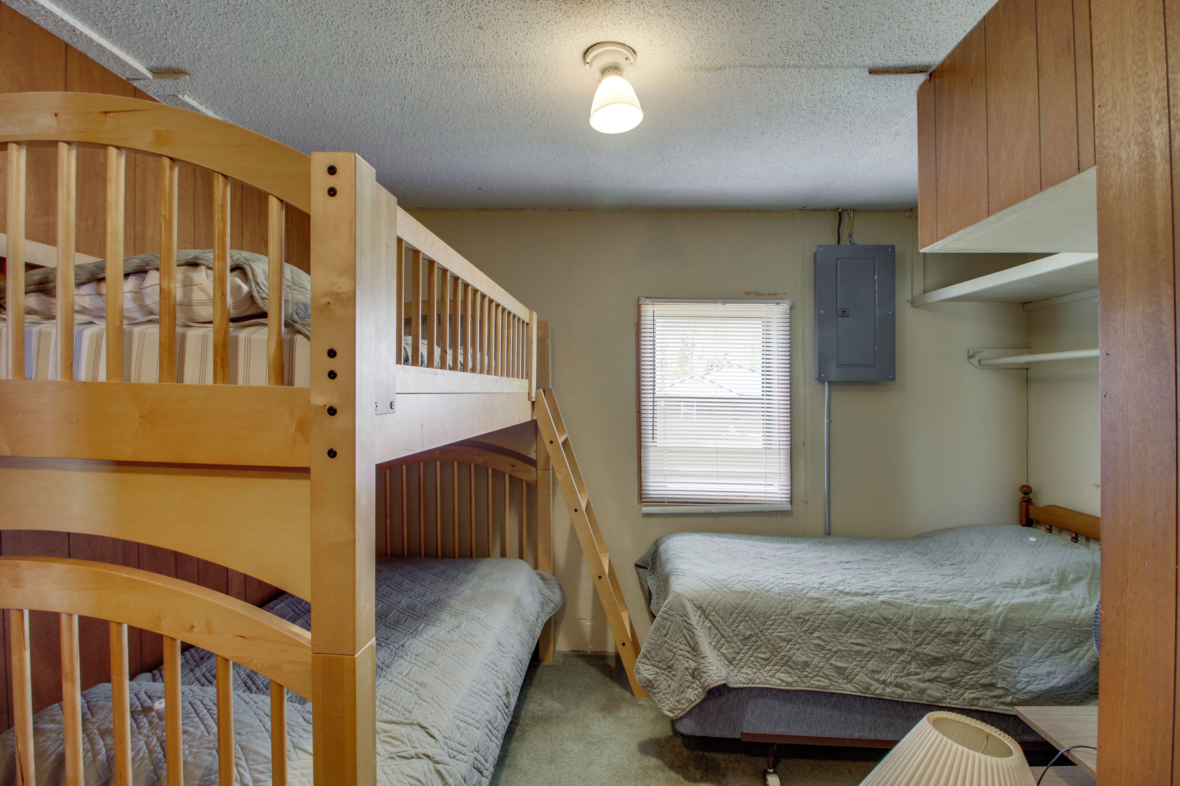 A bunk bed room with a window, a wall-mounted electrical box, and a bedside table.