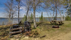 Ein Campingplatz am Seeufer mit Grill, Picknicktisch und Feuerstelle.