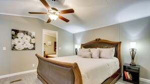 A bedroom with a wooden bed, a ceiling fan, a nightstand with a lamp, and a painting on the wall. - The Quiet Escape… Near New Orleans (LaPlace)
