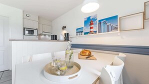 A modern kitchen with white cabinetry, a microwave, a kettle, and a dining area with a table set for two.