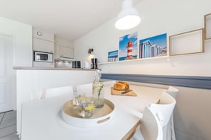 A modern kitchen with white cabinetry, a microwave, a kettle, and a dining area with a table set for two. - 2-Bedroom Beach Cottage (Fort Mahon Plage)