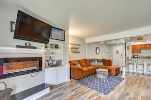 Ein Wohnzimmer mit Kamin, Fernseher, einer Couch und einer Küchenzeile mit Barhocker.