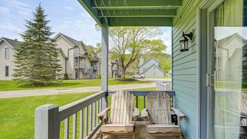 A porch with two wooden Adirondack chairs, a green awning, and a view of a residential street with houses and a tree.