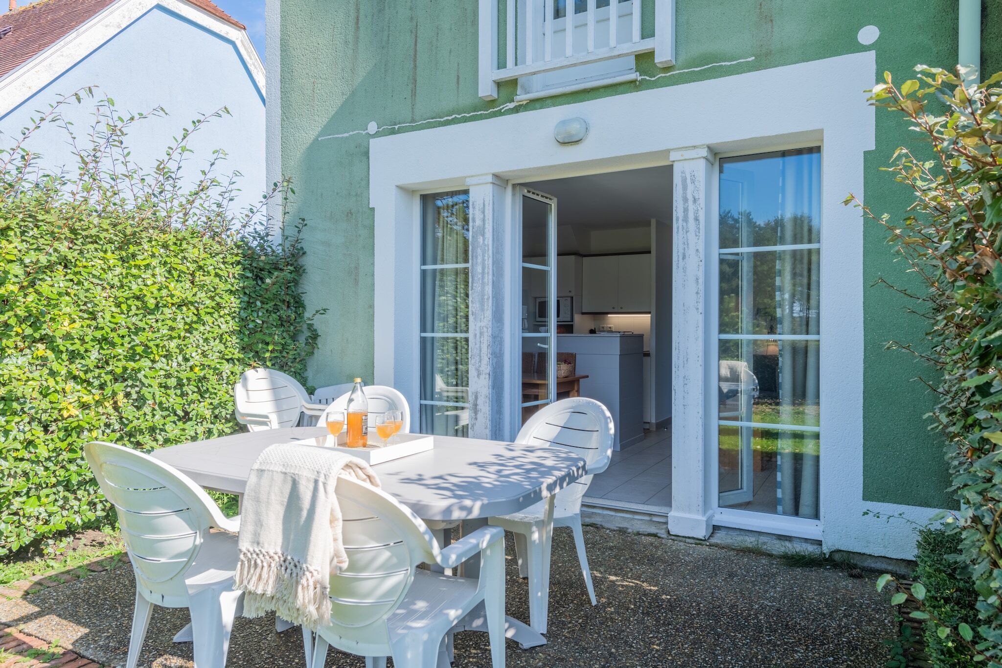A white table with chairs and a tablecloth outside a building with a green exterior and white trim.