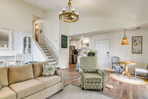 Ein Wohnzimmer mit Sofa, Sessel und Esstisch, eine Treppe und eine Küche im Hintergrund.