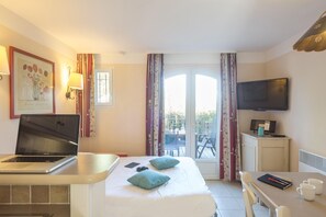 A hotel room with a bed, a desk with a laptop, a TV, and a balcony with curtains. - Family Apartment for 4 in Ardèche (Grospierres)