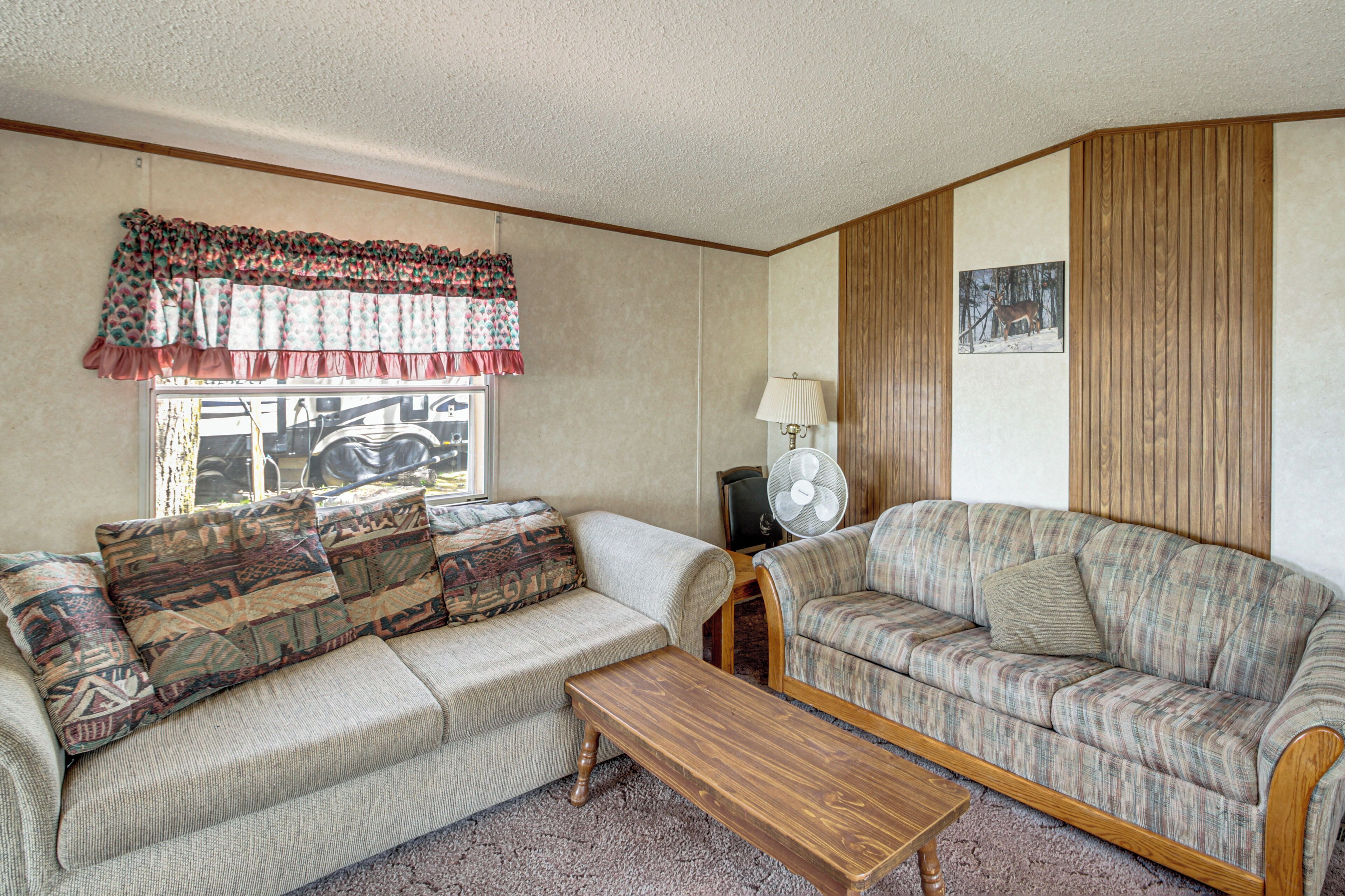 A living room with two sofas, a wooden coffee table, a lamp, a window with curtains, and a wall-mounted picture.