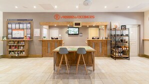 Un espace d’accueil comprenant un bureau en bois, deux tabourets de bar, un téléviseur, un tableau d’affichage et une étagère contenant divers objets.