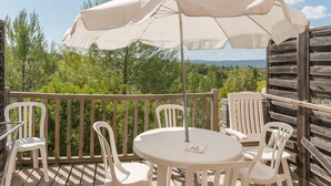 Un balcon avec une table et des chaises, un parasol blanc et une vue sur les arbres et les montagnes.