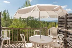 Un balcon avec une table et des chaises, un parasol blanc et une vue sur les arbres et les montagnes.
