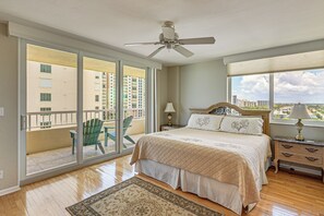Ein Schlafzimmer mit Bett, Nachttisch, Lampe, Deckenventilator, Fenster mit Aussicht und Balkon mit Stuhl.