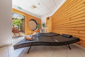 Ein Raum mit Holzwandverkleidung, einer Massageliege, einem Sessel und einem Blumentopf.