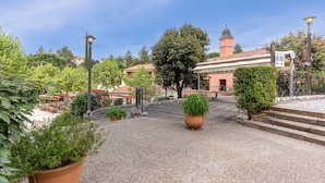 A courtyard with a gravel path, potted plants, and a building with a clock tower. - Ardèche House with Spacious Terrace for 8 (Grospierres)
