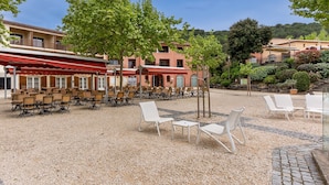 A courtyard with outdoor seating, a building with a red awning, and trees. - Ardèche House with Spacious Terrace for 8 (Grospierres)