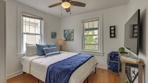 A bedroom with a bed, a ceiling fan, a window, a wall-mounted TV, and a small table with books. - Steps to Beach, Boardwalk & Eats! Ocean Grove Unit (Ocean Grove)