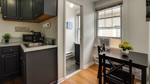 A kitchen with dark cabinets, a microwave, a sink, and a dining area with a table and chairs. - Steps to Beach, Boardwalk & Eats! Ocean Grove Unit (Ocean Grove)