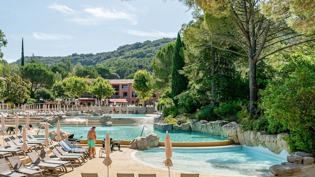 Zona de piscina con sillas de descanso, sombrillas y vistas a una colina.
