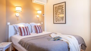 A hotel room with a bed, two wall-mounted lamps, an air conditioner, and a framed artwork. - Chic Riverfront Stay with Terrace (Mallemort)