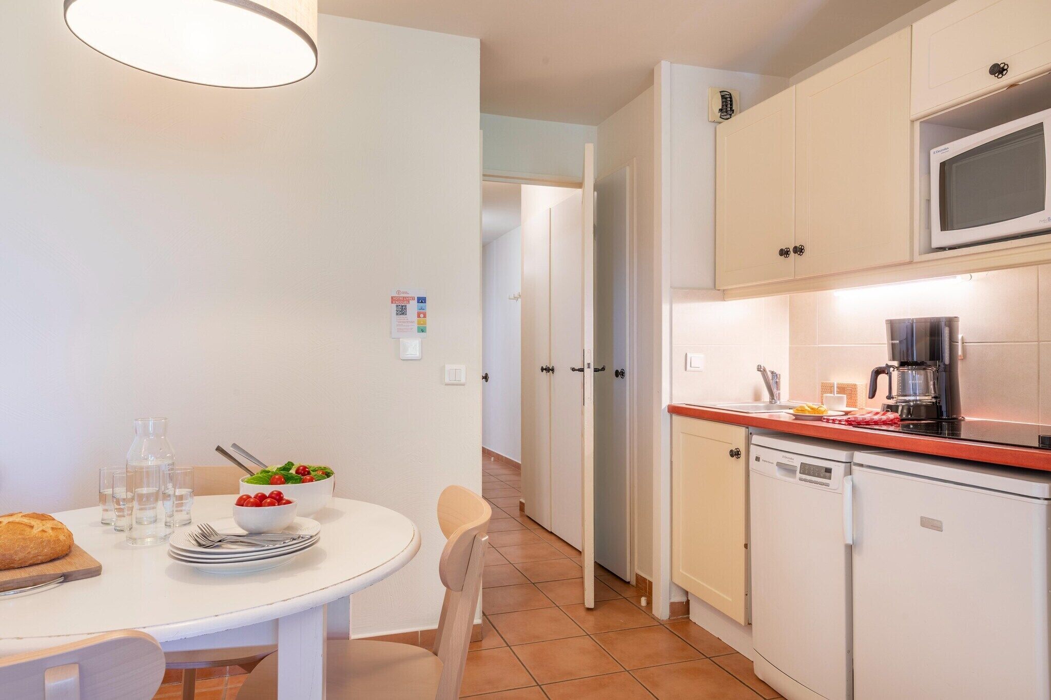 Cocina compacta con microondas, cafetera y lavavajillas. Se ha dispuesto una mesa con platos y vasos.