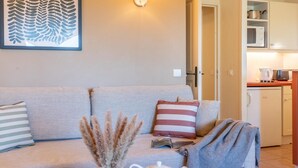 Ein Wohnzimmer mit einer Couch, Kissen, einer Vase mit Trockenpflanzen, einer Teekanne und einer Decke.