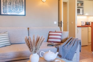 Een woonkamer met een bank, kussens, een vaas met gedroogde planten, een theepot en een plaid.