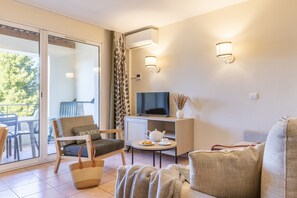 Un salon moderne avec un canapé, un fauteuil, une télévision et une petite table sur laquelle se trouve une théière.