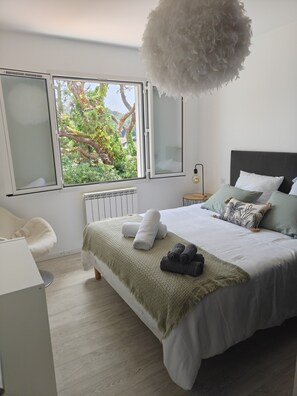 Ein modernes Schlafzimmer mit einem großen Bett, Blick ins Grüne, einem Heizkörper und einer weißen, flauschigen Lampe.
