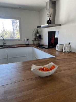 Eine moderne Küche mit einer Holzarbeitsplatte, einer weißen Schale mit Orangen, einer Kaffeemaschine und einem Toaster.
