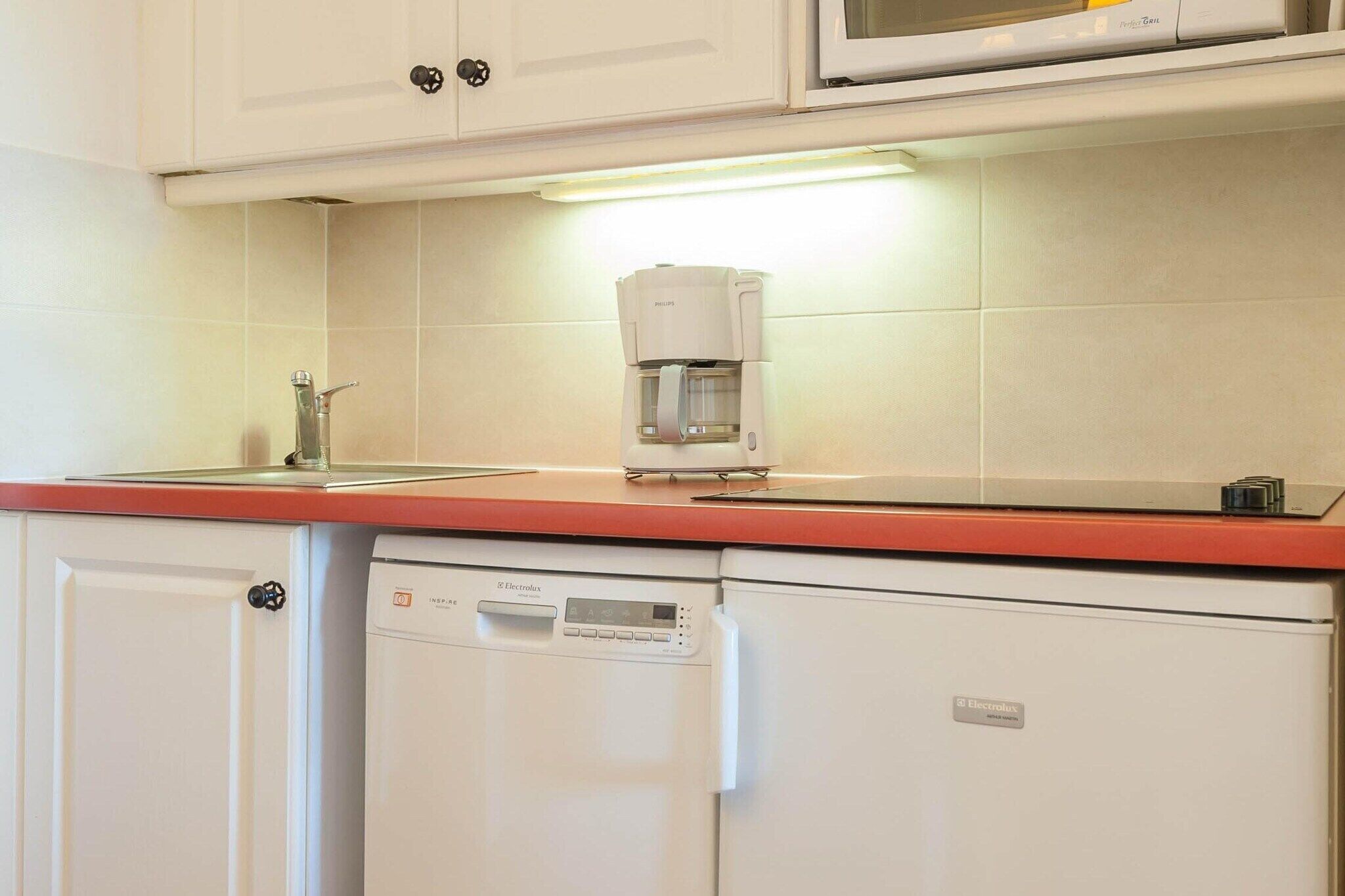 Una cocina equipada con cafetera, lavavajillas y microondas.