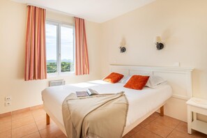 A bedroom with a bed, a window with curtains, a bedside table, and a wall-mounted lamp. - Apartment with Wave Pools Access (Mallemort)