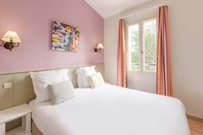 Une chambre à coucher avec un lit, deux tables de chevet, une lampe fixée au mur, une fenêtre avec des rideaux et une œuvre d’art colorée accrochée au mur.