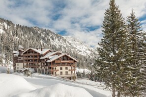 A multi-story lodge with a wooden facade, surrounded by snow-covered mountains and trees. - Retreat with Spa Access (Flaine)