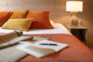 Ein ordentlich bezogenes Bett mit orangefarbener Bettwäsche, eine Nachttischlampe, ein Buch und ein Stift auf dem Nachttisch.