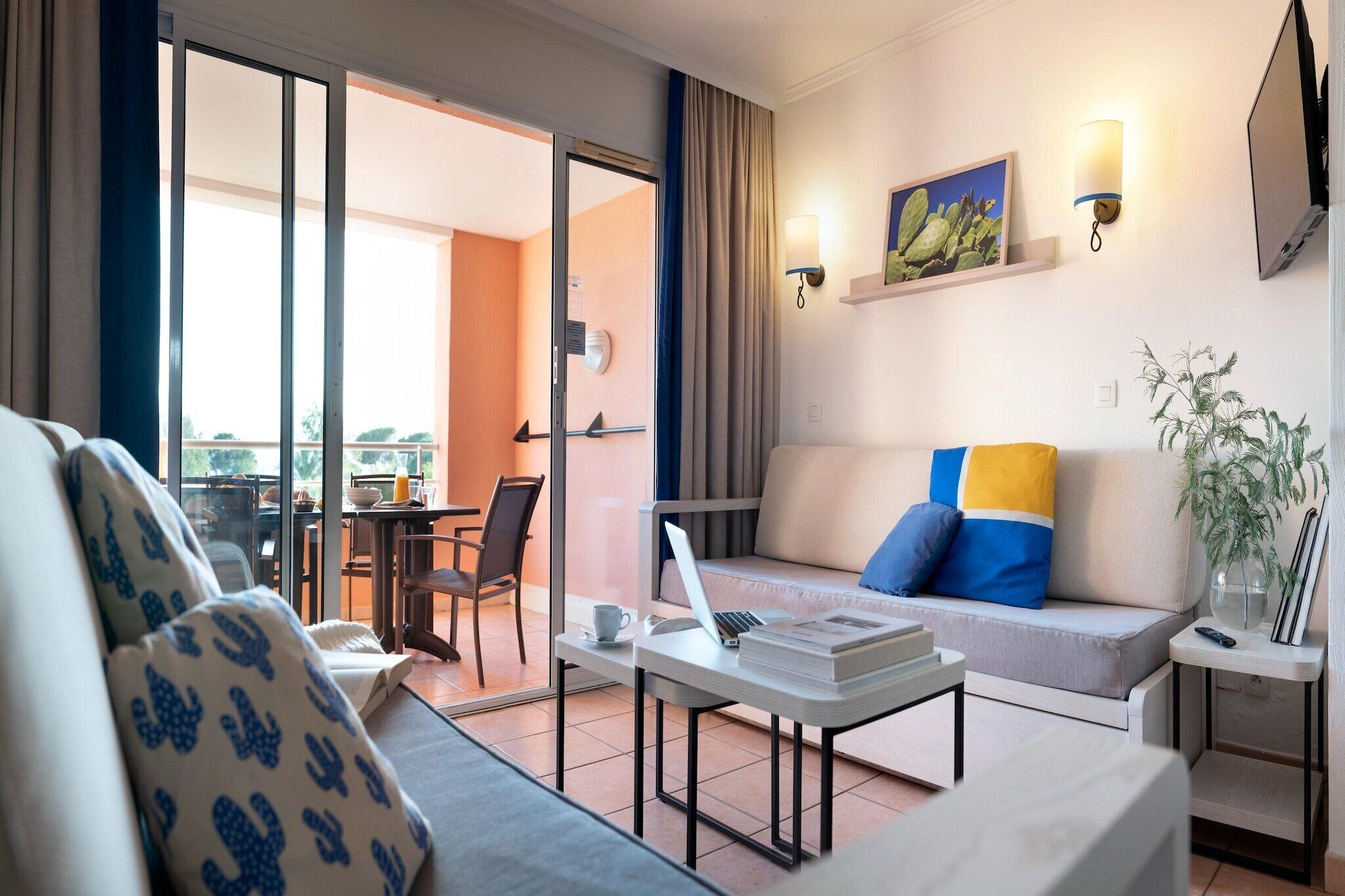 Une chambre d’hôtel avec un canapé, une table basse, un ordinateur portable, une télécommande et une plante.