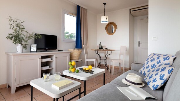 A living room with a sofa, a television, a dining table, and a small kitchen area. - Stunning 4-Person Sea View Haven (Les Issambres)