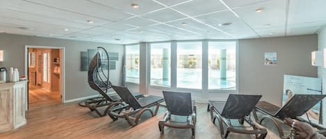 A room with wooden flooring, ceiling lights, and large windows.