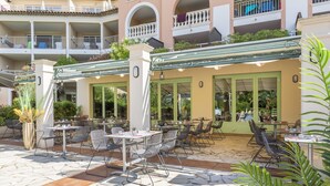 An outdoor patio with tables and chairs, a covered seating area, and a building with balconies in the background. - Stunning 4-Person Sea View Haven (Les Issambres)