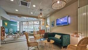 A lobby with wicker chairs, a green sofa, and a television mounted on the wall. - Courseulles Family Apartment for 6 (COURSEULLES SUR MER)