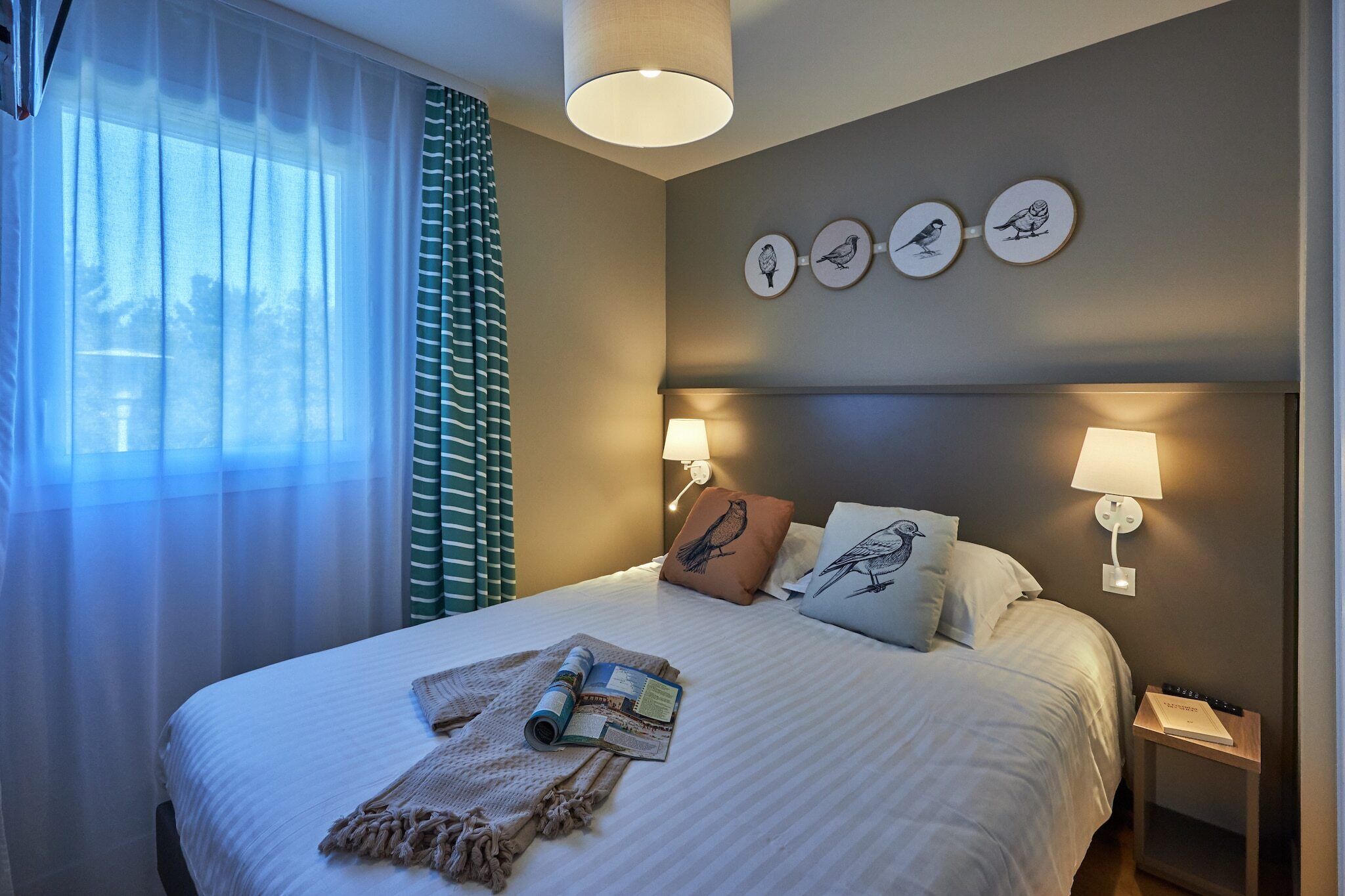 Un lit bien fait, avec des oreillers, une table de chevet avec une lampe et des œuvres d’art accrochées au mur.