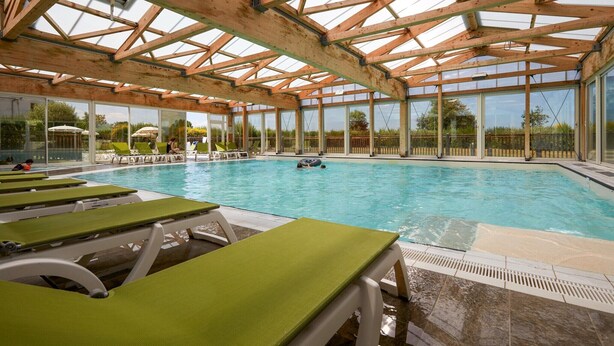 An indoor swimming pool with wooden beams, clear glass walls, and green lounge chairs. - Courseulles Family Apartment for 6 (COURSEULLES SUR MER)