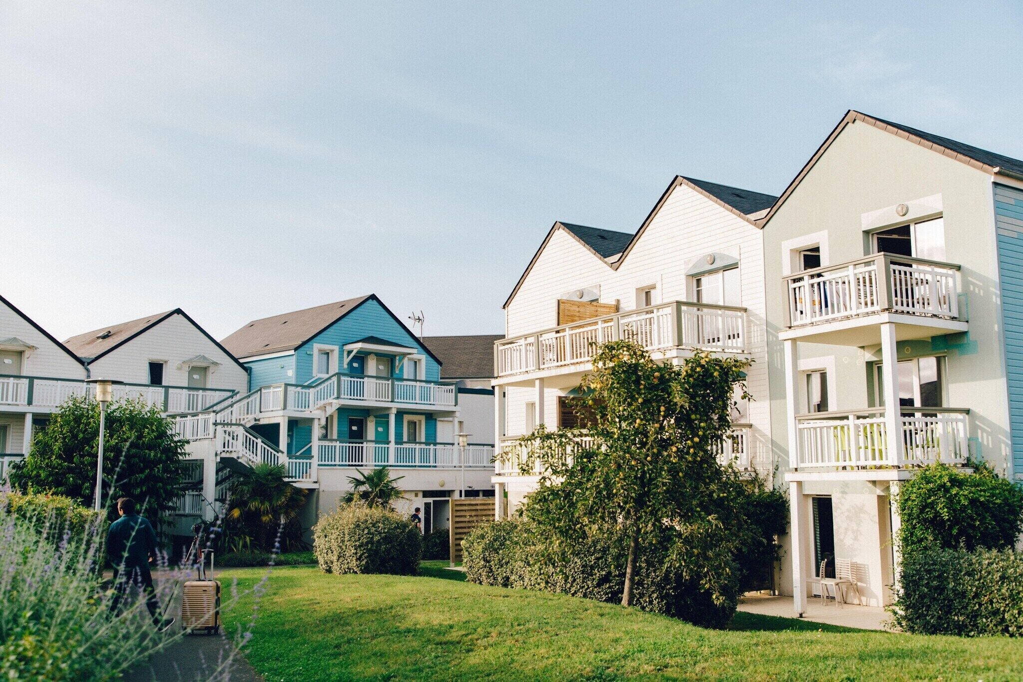 A row of multi-story residential buildings with balconies, a grassy area, and a pathway.