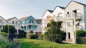 A row of multi-story residential buildings with balconies, a grassy area, and a pathway. - Courseulles Family Apartment for 6 (COURSEULLES SUR MER)