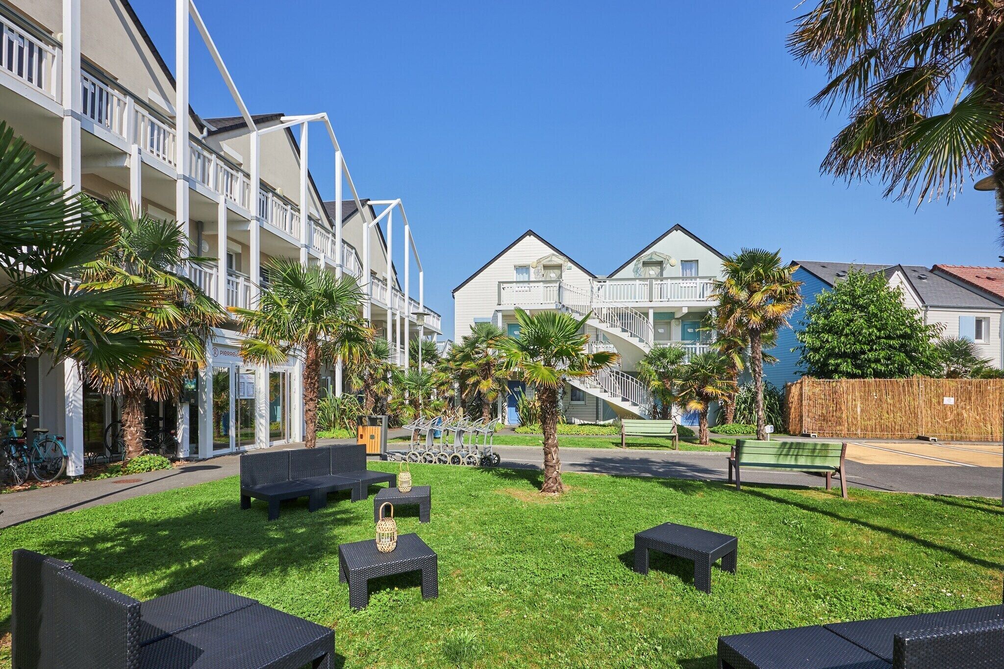 A courtyard with outdoor seating, a palm tree, and a building with balconies.